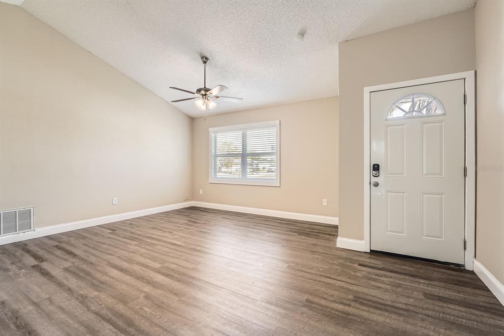 7001 Heath Drive Port Richey, FL 34668 - Photo 2 of 11 an empty room with wooden floor chandelier fan and windows