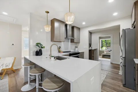a kitchen with stainless steel appliances kitchen island granite countertop a sink a refrigerator a stove a dining table and chairs with wooden floor