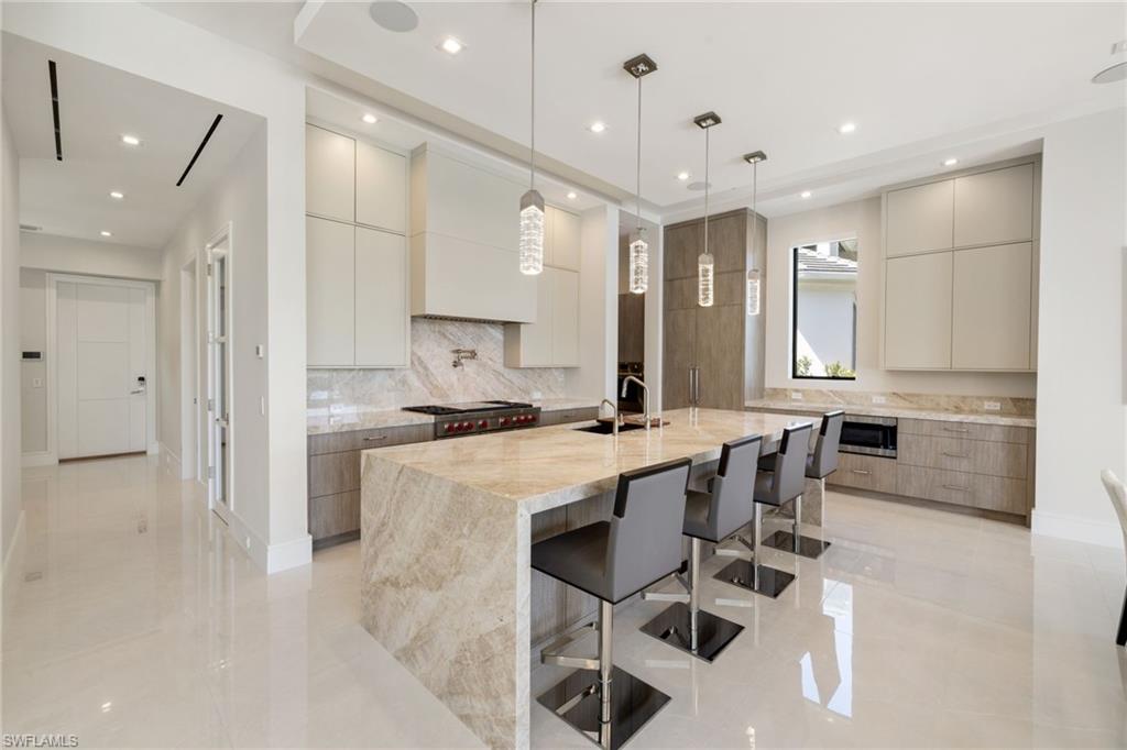 2345 Tarpon Road Naples, FL 34102 - Photo 12 of 43 Dual tone kitchen featuring modern cabinets, light stone counters, dual tone cabinetry, an island with sink, and pendant lighting