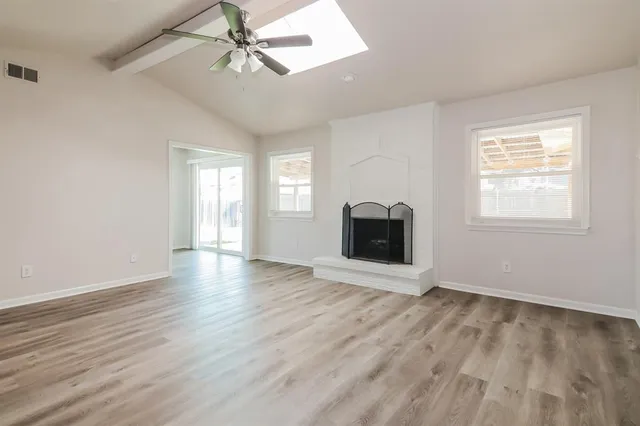 an empty room with wooden floor fireplace and windows