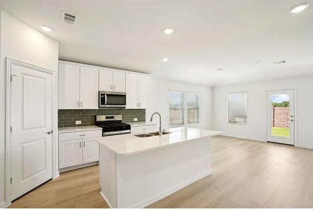 a kitchen with stainless steel appliances a sink a stove a microwave a center island and cabinets