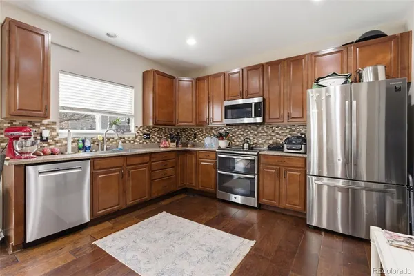 a kitchen with stainless steel appliances granite countertop a refrigerator a sink dishwasher a stove with wooden cabinets and wooden floor