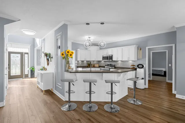 a kitchen with stainless steel appliances granite countertop a refrigerator a sink dishwasher a stove top oven a dining table and chairs with wooden floor