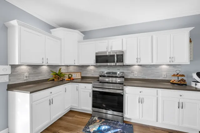 a kitchen with granite countertop a stove a sink dishwasher a refrigerator and white cabinets with wooden floor