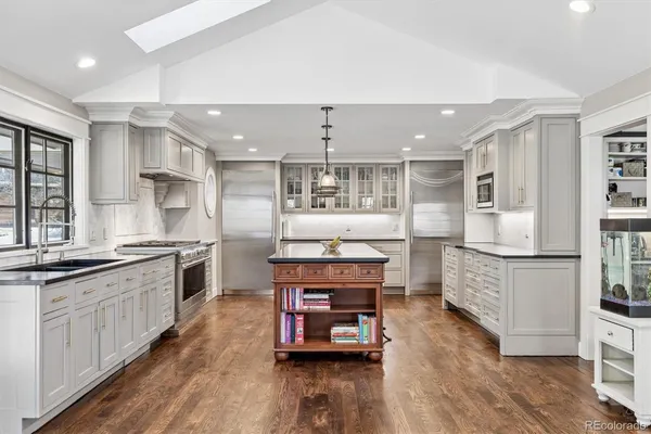 a large kitchen with stainless steel appliances kitchen island granite countertop a large stove a refrigerator a sink a dining table and chairs with wooden floor