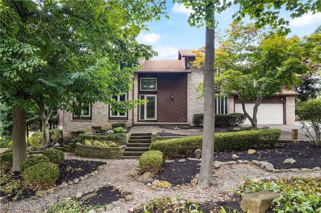 Mid-century home featuring brick siding, a garage, a shingled roof, and driveway