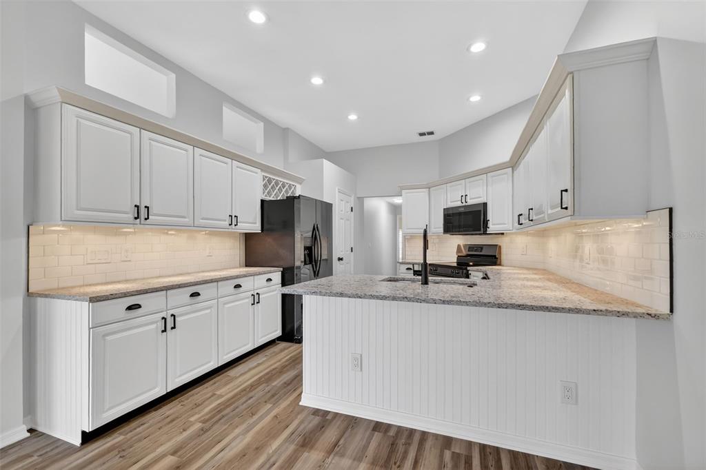 6027 Spring Creek Court Mount Dora, FL 32757 - Photo 12 of 42 a large kitchen with stainless steel appliances granite countertop a stove a sink a refrigerator and white cabinets with wooden floor