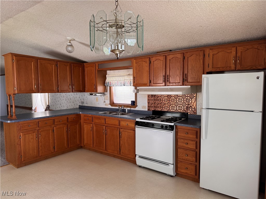 5852 Cleveland Road, Unit 104 Wooster, OH 44691 - Photo 9 of 36 Kitchen featuring white appliances, under cabinet range hood, a sink, brown cabinets, and dark countertops