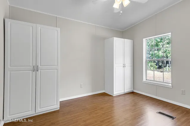 an empty room with wooden floor chandelier fan and windows