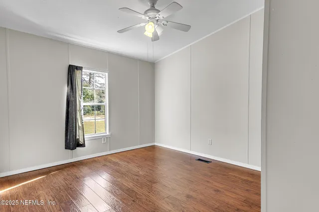 an empty room with wooden floor chandelier fan and windows