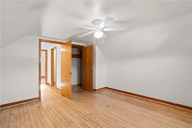 a view of an empty room with wooden floor and a ceiling fan