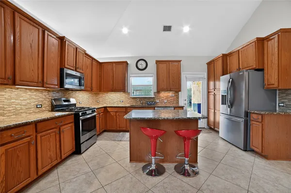 a kitchen with stainless steel appliances granite countertop a stove top oven a refrigerator a sink and dishwasher with wooden cabinets