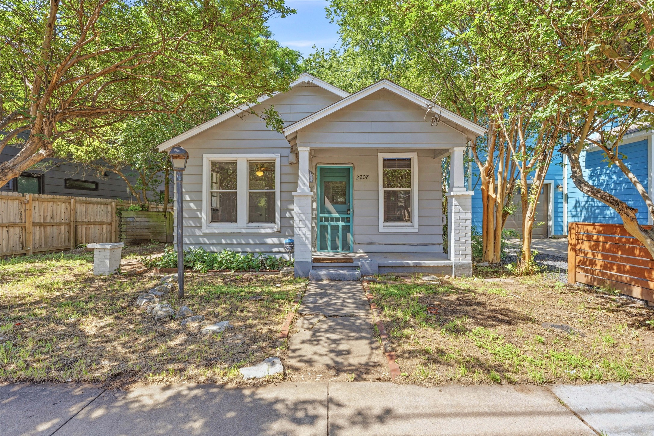 2207 Santa Rita Street Austin, TX 78702 - Photo 1 of 15 Charming single-story residence featuring a covered front porch with stone-clad columns, a vibrant teal front door, and a light gray siding exterior