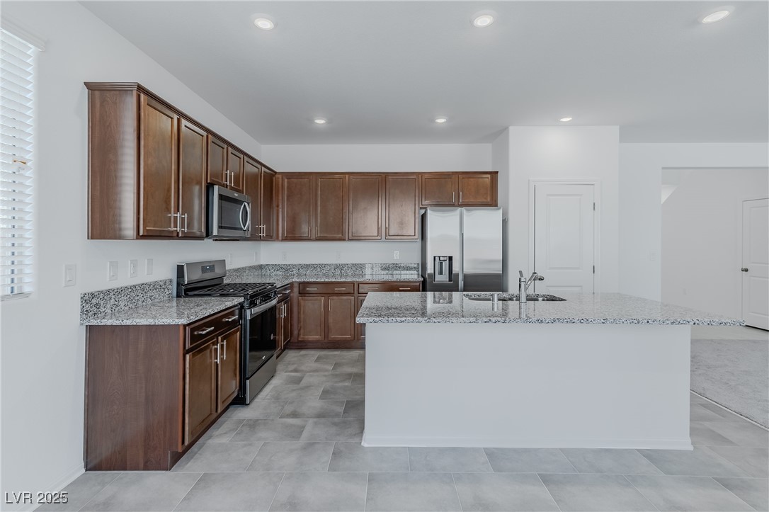 7859 Lacemaker Court Las Vegas, NV 89113 - Photo 6 of 24 Kitchen with stainless steel appliances, light stone countertops, a kitchen island with sink, dark brown cabinets, and recessed lighting