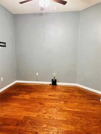 a view of an empty room with wooden floor and fan