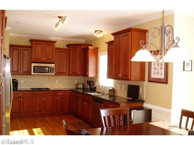8052 Glengarriff Road Clemmons, NC 27012 - Photo 2 of 16 Kitchen. Stainless steel, tille back splash, granite, hardwoods, crown molding, chair rail, and shadow box accents. The cook top is gas, the wood on the cabinets warm, and space is remarkable.
