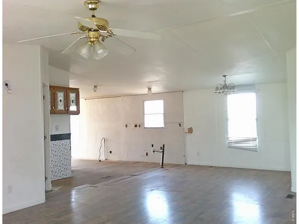 an empty room with wooden floor chandelier fan and windows