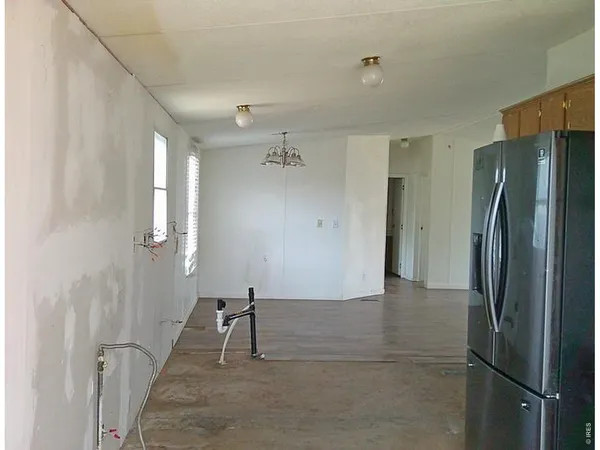 a view of a refrigerator in kitchen and an empty room with wooden floor