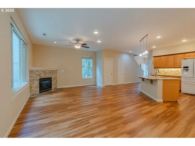 a view of an empty room with wooden floor and a kitchen