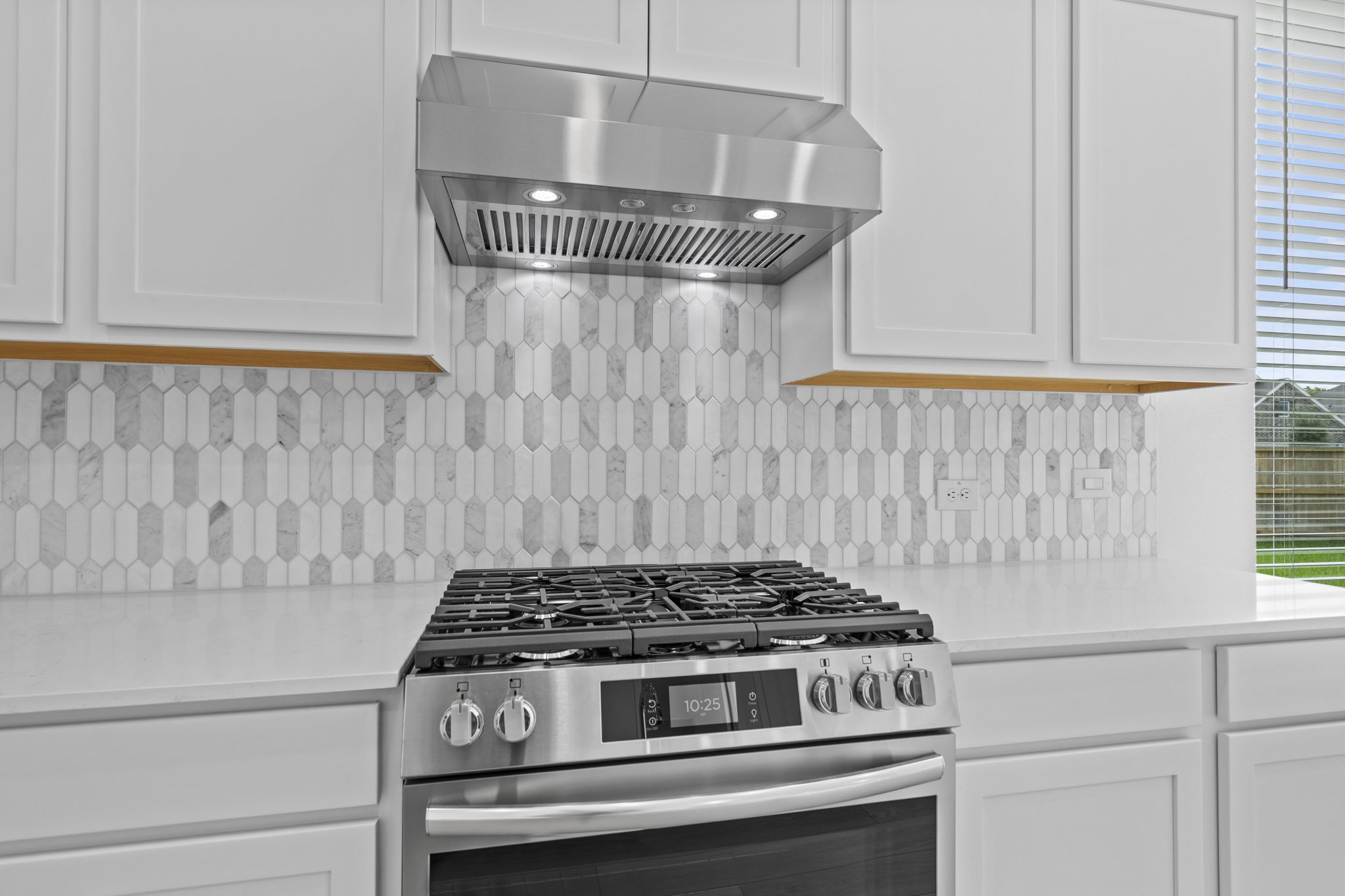 2720 Grove Crest Drive Rosenberg, TX 77469 - Photo 12 of 32 This kitchen features a modern stainless steel gas stove with a sleek range hood and under-cabinet lighting. The backsplash is a stylish geometric pattern, complemented by white cabinetry and quartz countertops. Perfect for a contemporary home.