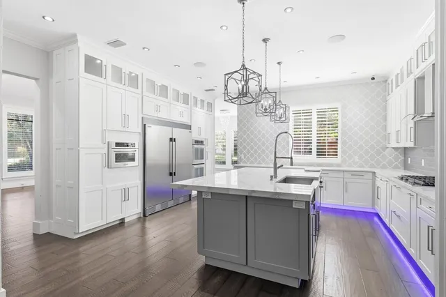 a kitchen with stainless steel appliances a sink dishwasher a refrigerator a stove and white cabinets with wooden floor