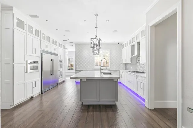 a kitchen with stainless steel appliances a stove a sink dishwasher a refrigerator and white cabinets with wooden floor