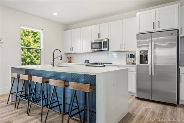 a kitchen with stainless steel appliances granite countertop a refrigerator a sink a stove a dining table and chairs