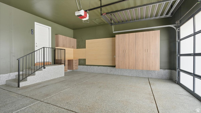 2038 East Ranch Road Eagle Mountain, UT 84005 - Photo 40 of 66 Spacious garage featuring a finished epoxy floor, built-in wood-finish cabinetry, slat wall storage system, an overhead storage rack, and a glass-paneled garage door