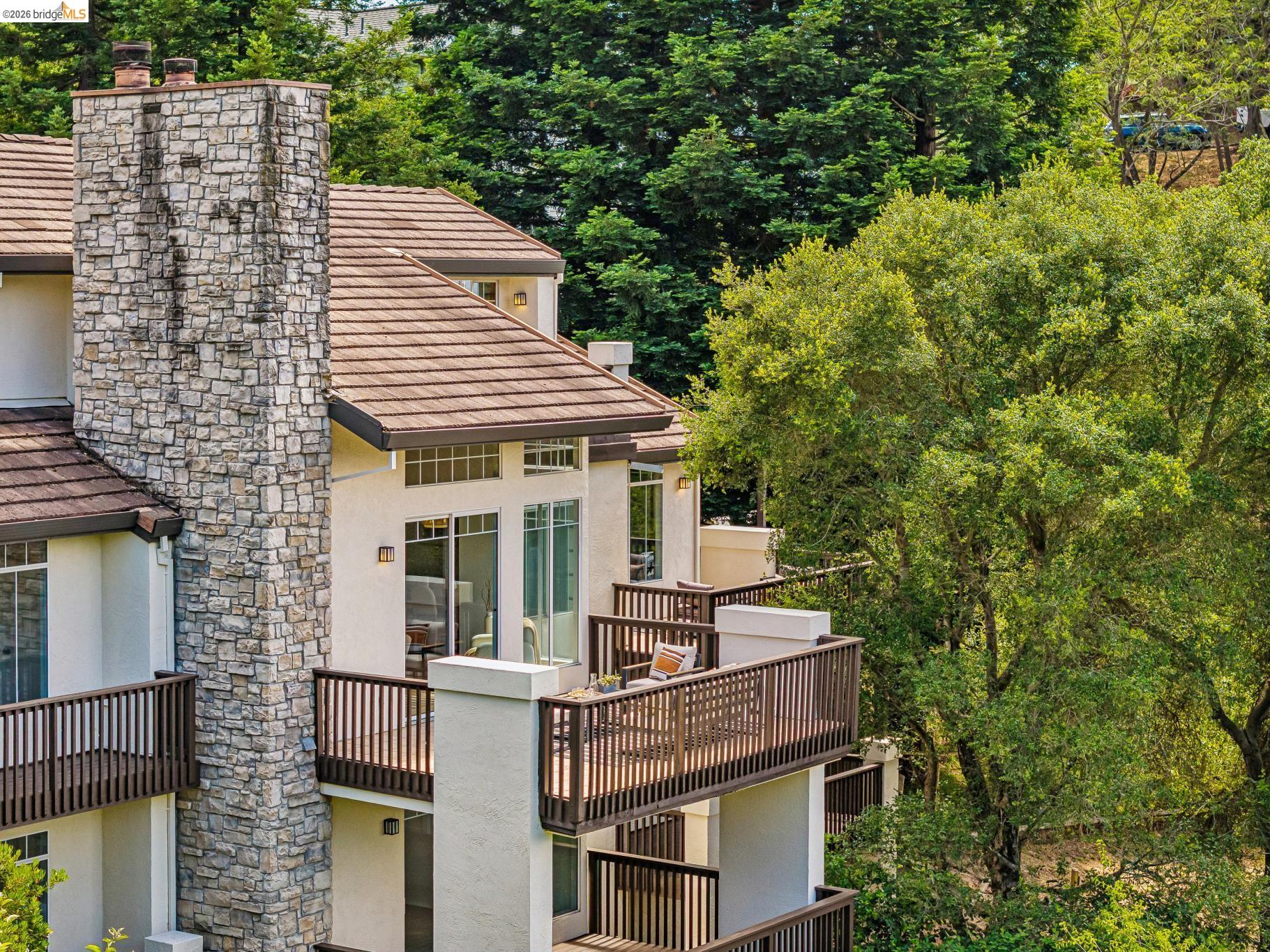1325 Drury Road Berkeley, CA 94705 - Photo 69 of 71 Exterior featuring a stone chimney, multiple balconies with wood railings, stucco siding, and a tiled roof, surrounded by mature trees