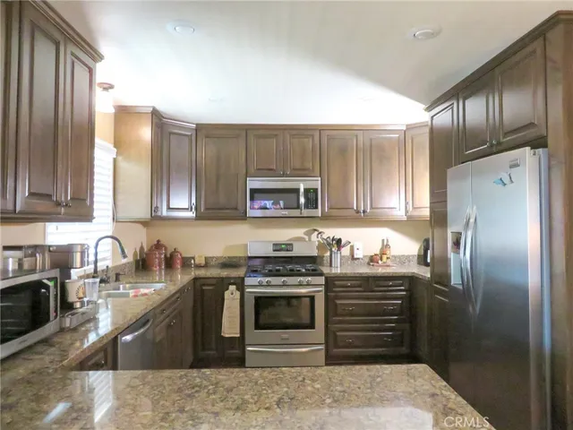 a kitchen with stainless steel appliances granite countertop a refrigerator a stove a sink and a microwave