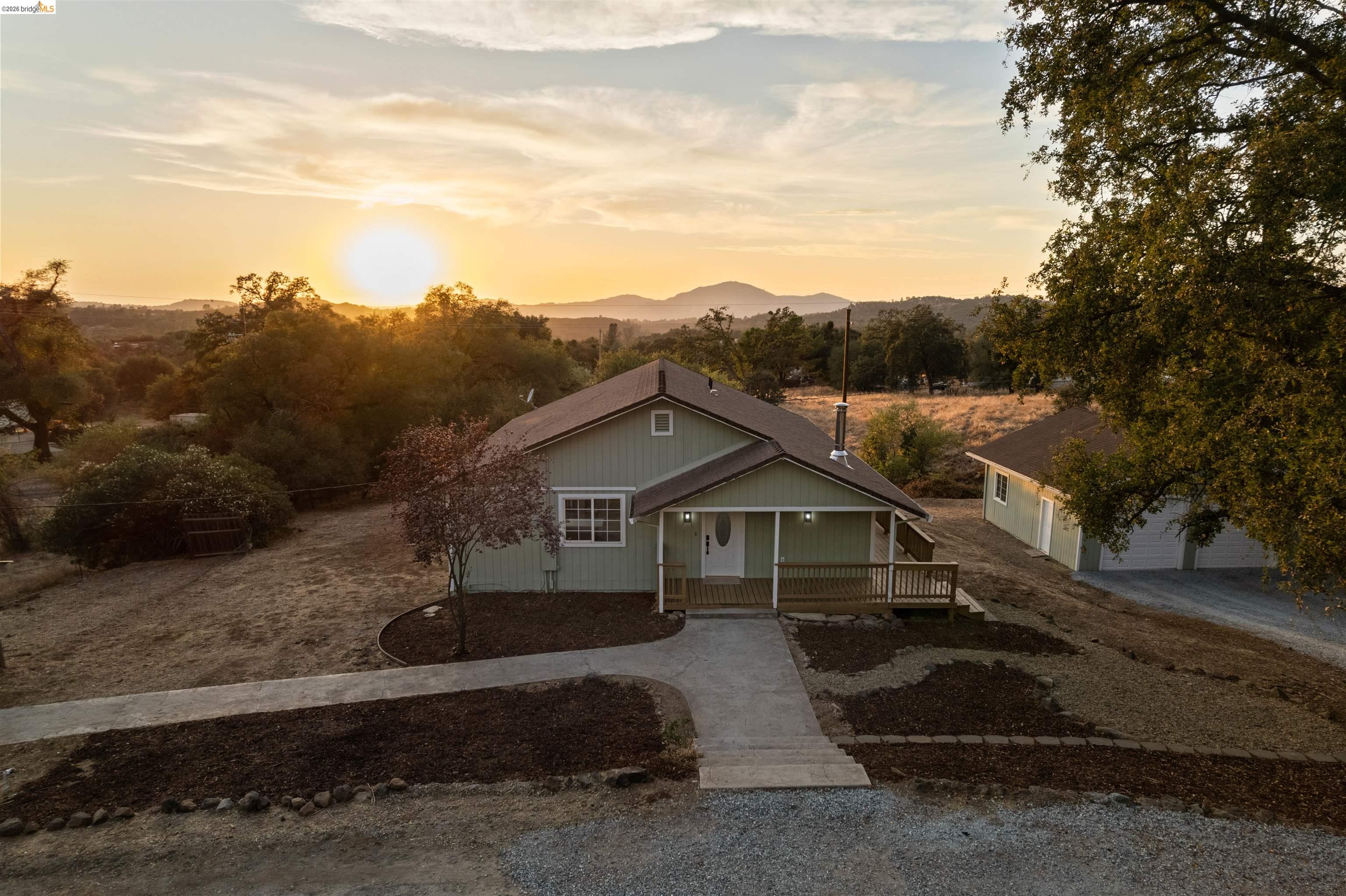 19676 Rawhide Road Sonora, CA 95370 - Photo 60 of 67 Light green exterior with white trim, covered front porch with wood railing, paved walkway, gravel driveway, and a detached garage structure