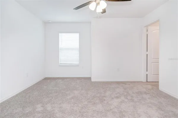 an empty room with a ceiling fan and kitchen view