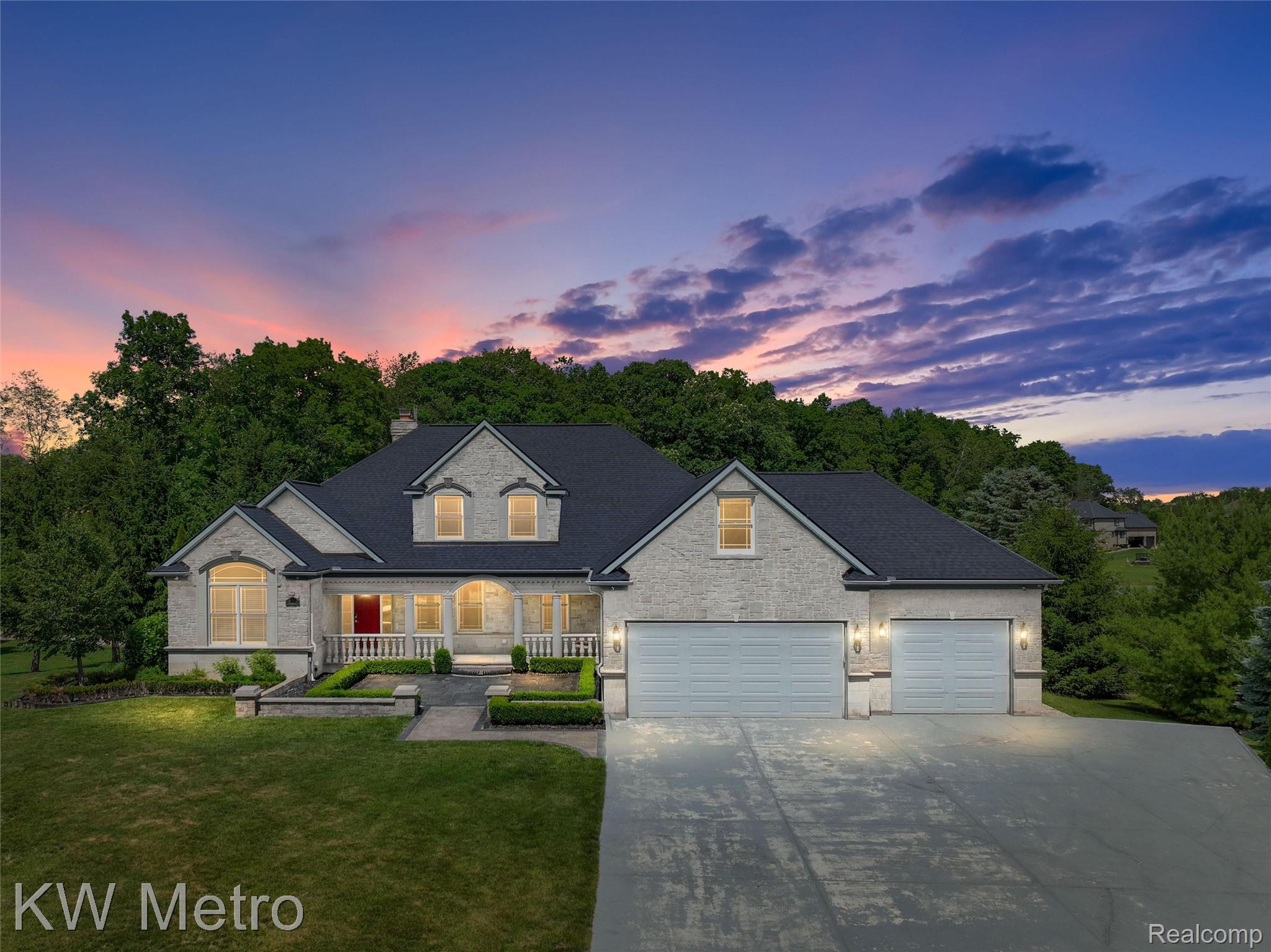 65884 Windrose Court Ray, MI 48096 - Photo 1 of 82 Stone veneer exterior featuring a two-car garage, dormer windows, and a covered front porch with balustrade