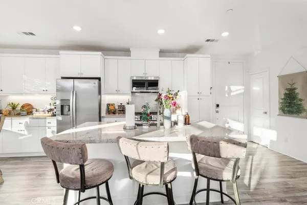 a kitchen with stainless steel appliances kitchen island granite countertop a dining table chairs refrigerator and microwave