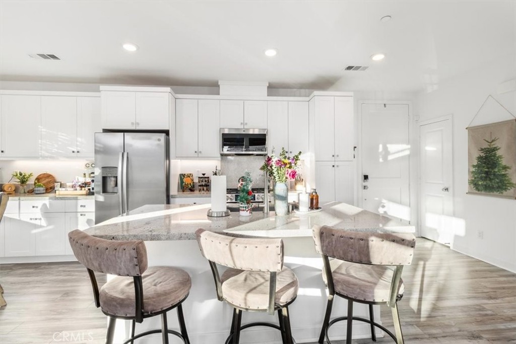 a kitchen with stainless steel appliances kitchen island granite countertop a dining table chairs refrigerator and microwave