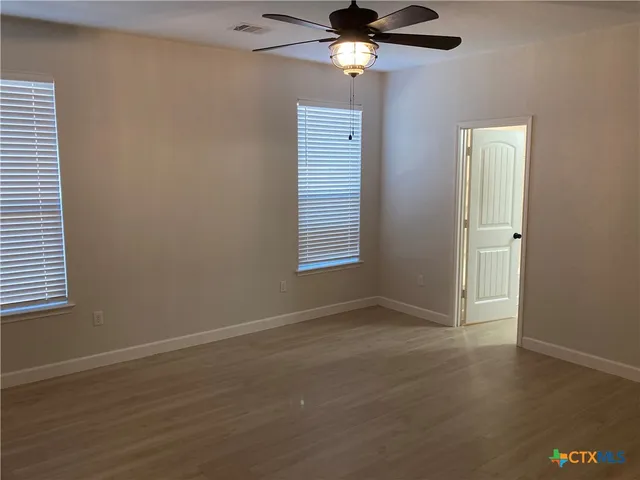 an empty room with wooden floor closet and windows