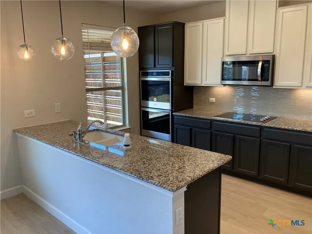 a kitchen with kitchen island granite countertop a sink cabinets and stainless steel appliances