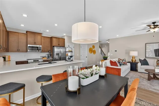 a living room with stainless steel appliances a dining table wooden floor windows and kitchen view