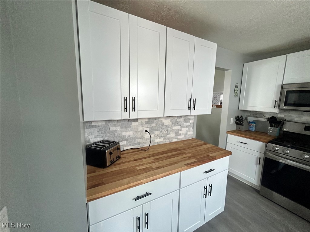 935 Lilly Road Alliance, OH 44601 - Photo 17 of 31 Kitchen with wooden counters, appliances with stainless steel finishes, backsplash, a textured ceiling, and white cabinets