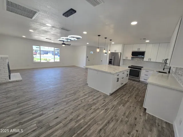a large white kitchen with kitchen island a stove a sink dishwasher and a fireplace with wooden floor