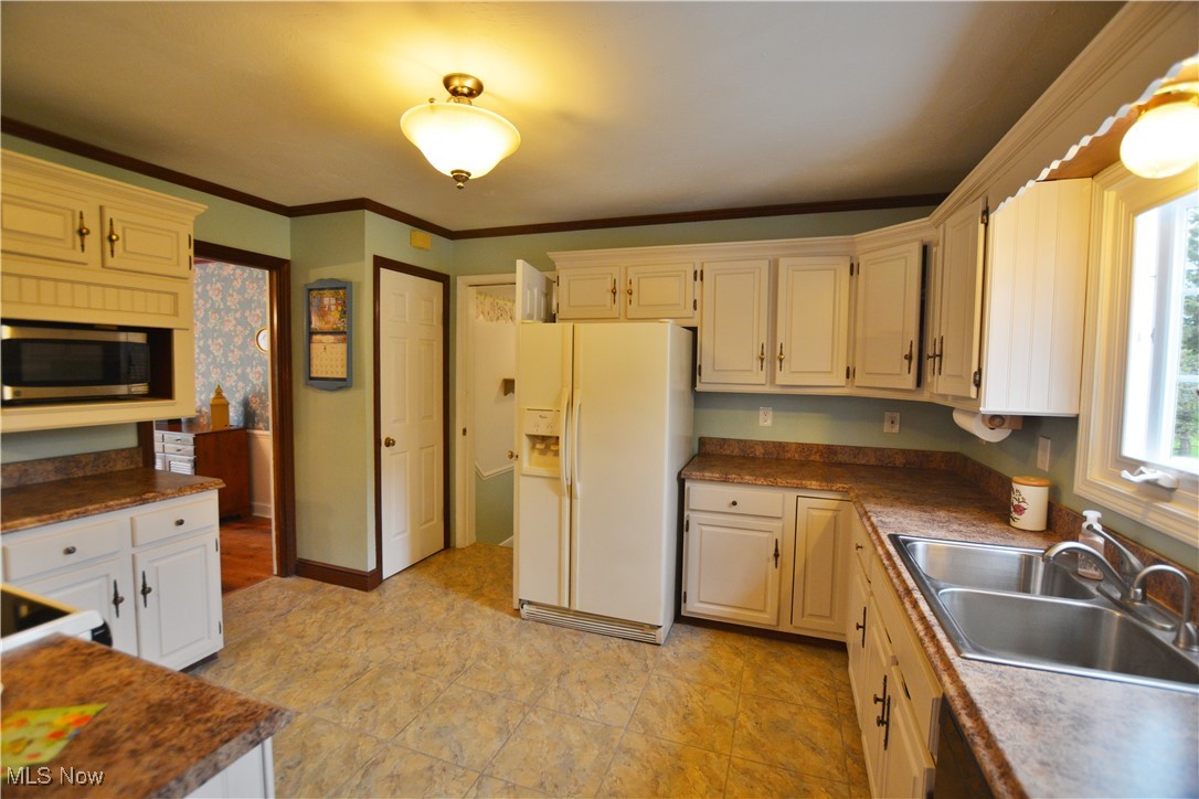 16140 Thompson Road Thompson, OH 44086 - Photo 26 of 50 Kitchen featuring white refrigerator with ice dispenser, stainless steel microwave, a sink, crown molding, and dark countertops