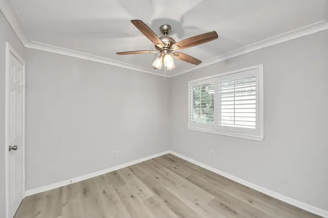 an empty room with wooden floor ceiling fan and window