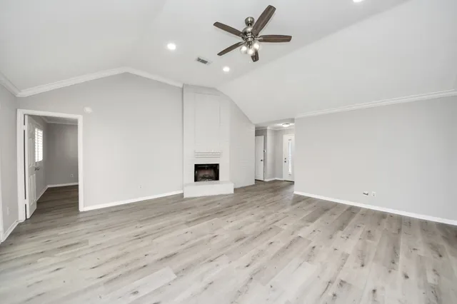 a view of an empty room with wooden floor and a ceiling fan
