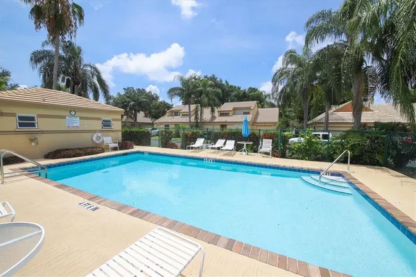 a view of a swimming pool with a lawn chairs under palm trees