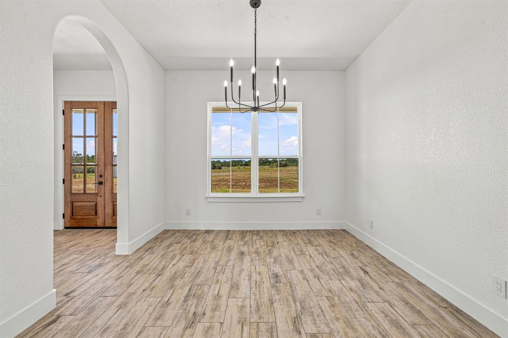 8140 Lavender Road Springtown, TX 76082 - Photo 9 of 40 Arched entryway leading to a wood-paneled door with glass inserts, wood-finish flooring, a contemporary chandelier, and a large window