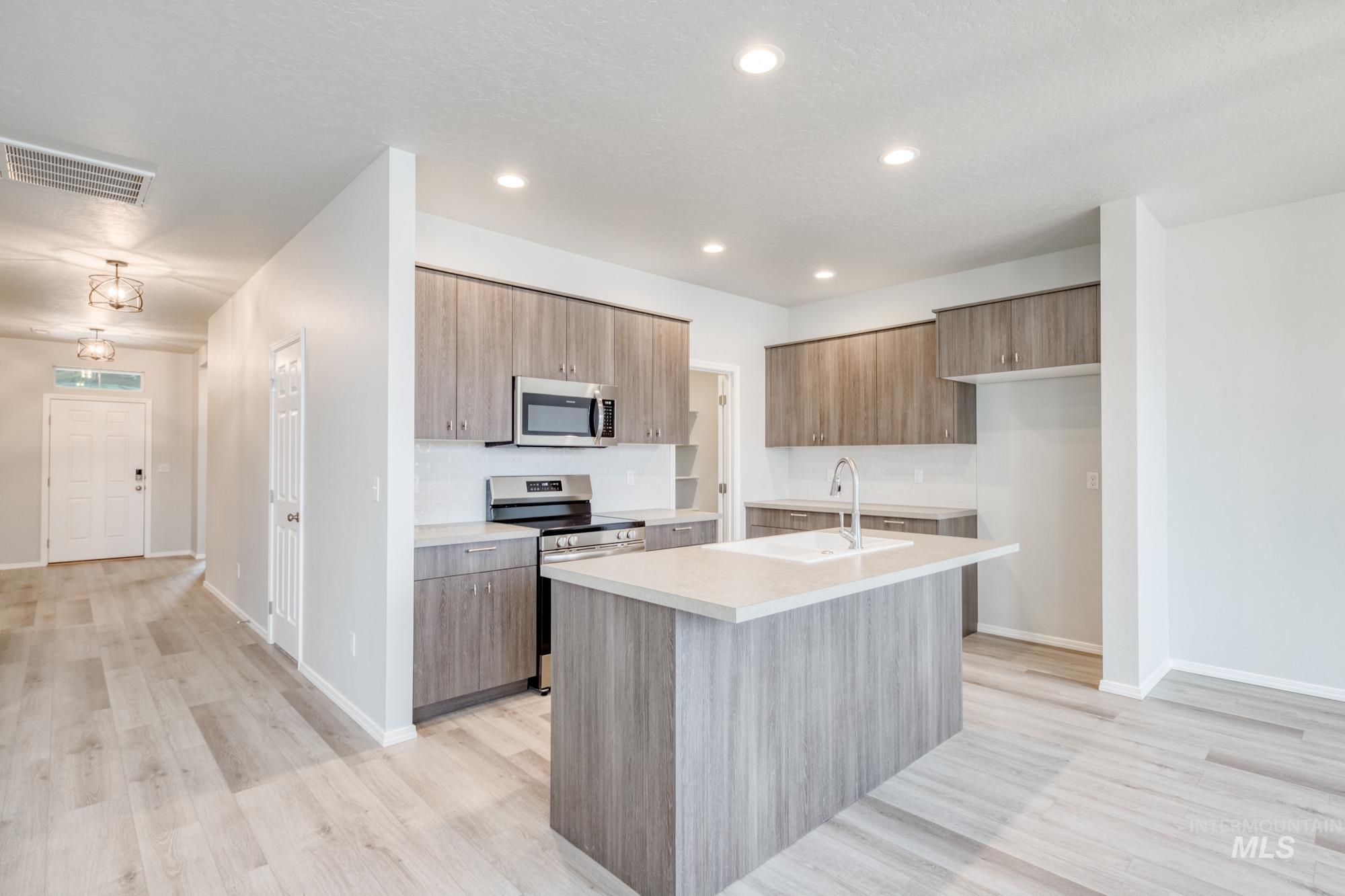 13740 Judson Street Caldwell, ID 83607 - Photo 3 of 23 Kitchen featuring stainless steel appliances, modern cabinets, light wood-style floors, a kitchen island with sink, and brown cabinetry
