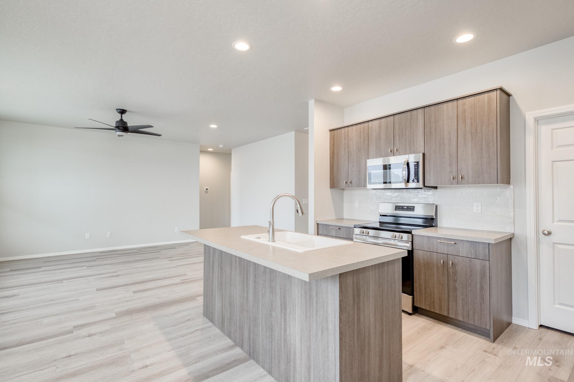 13740 Judson Street Caldwell, ID 83607 - Photo 5 of 23 Kitchen with appliances with stainless steel finishes, a kitchen island with sink, light countertops, light wood-style floors, and tasteful backsplash