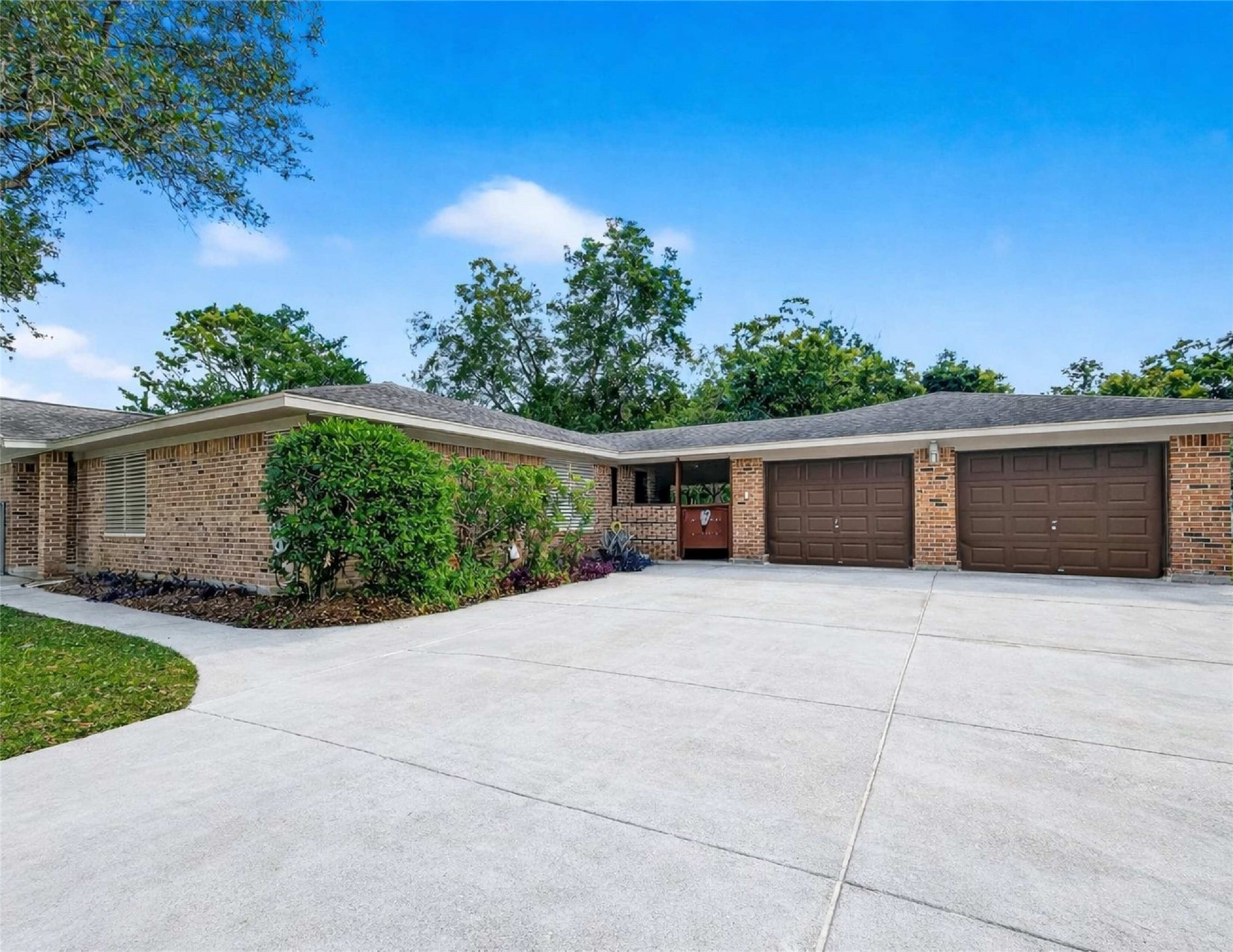 12021 7th 1/2 Street Santa Fe, TX 77510 - Photo 1 of 49 This photo showcases a spacious, single-story brick home with a two-car garage. The property features a large driveway, well-maintained landscaping, and is surrounded by mature trees, providing a serene and inviting atmosphere.