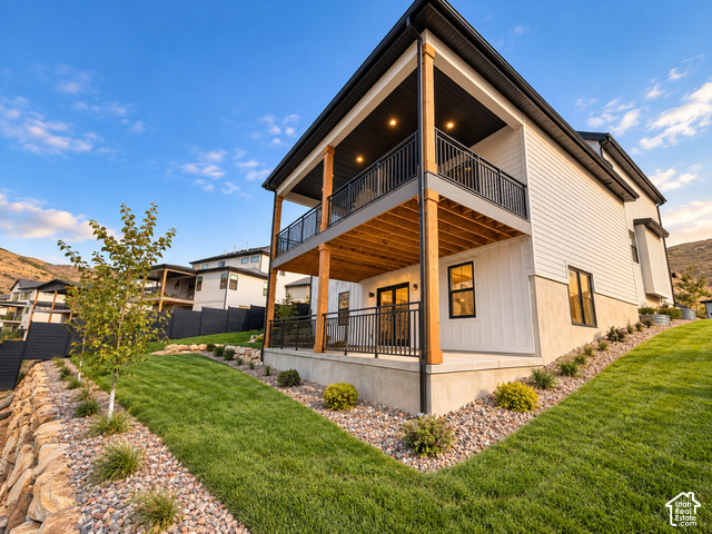 1595 West Canyon Rim Road, Unit 630 Lehi, UT 84048 - Photo 6 of 41 Modern exterior featuring white siding, a two-story covered deck with wood accents, and a manicured lawn with natural rock landscaping. Lighting enhanced with ai.