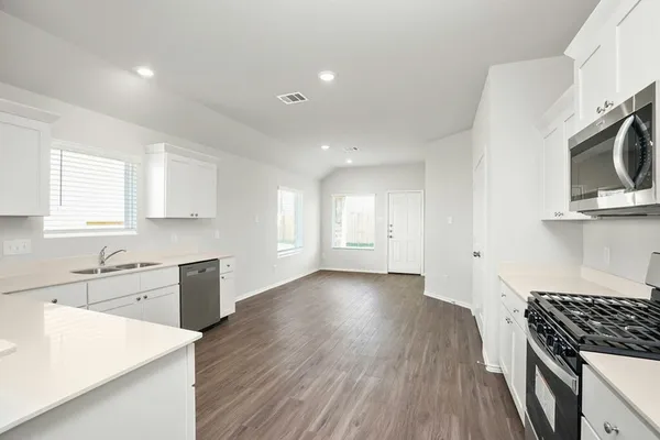 a kitchen with granite countertop a stove top oven a sink dishwasher and white cabinets with wooden floor